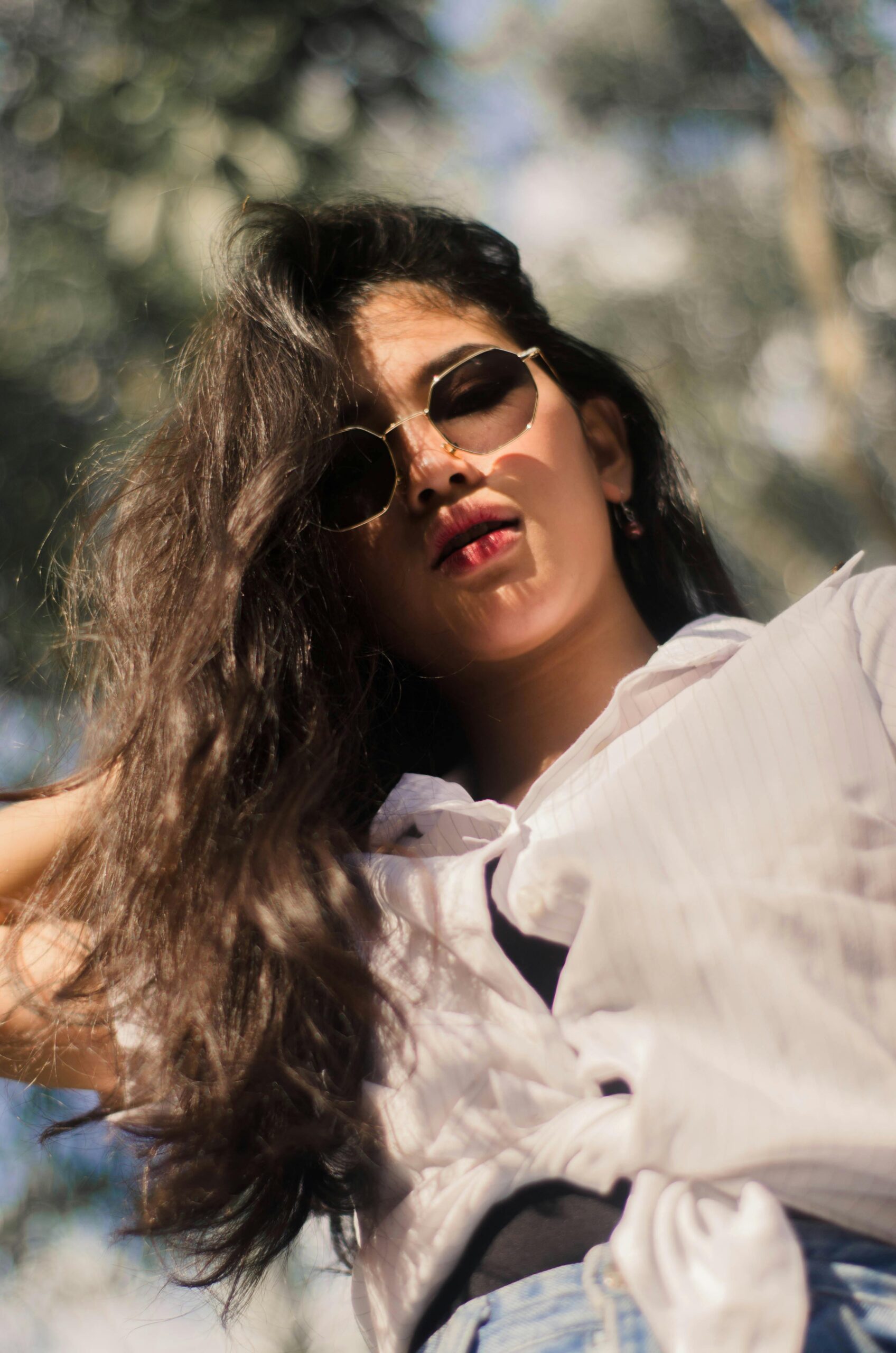 A fashionable woman wearing sunglasses poses confidently outdoors in natural light, exuding a modern aesthetic.